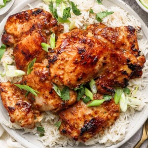 A plate of grilled chicken served on a bed of rice, garnished with chopped green onions and cilantro.