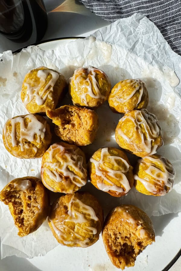 A plate of small, round pastries drizzled with white icing, some partially eaten, on a piece of parchment paper.