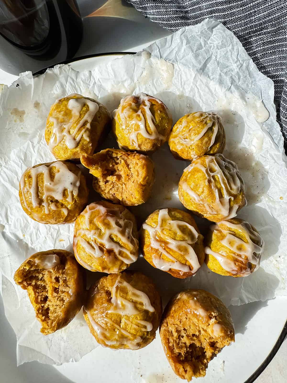 A plate of small, round pastries drizzled with white icing, some partially eaten, on a piece of parchment paper.