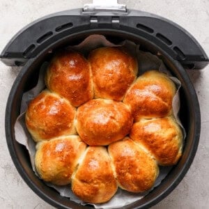 Golden brown homemade rolls arranged in a circular pattern inside an air fryer basket on a gray surface.