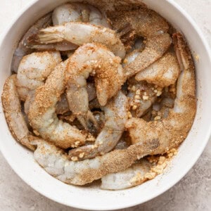 A bowl of raw shrimp seasoned with spices, ready for cooking.