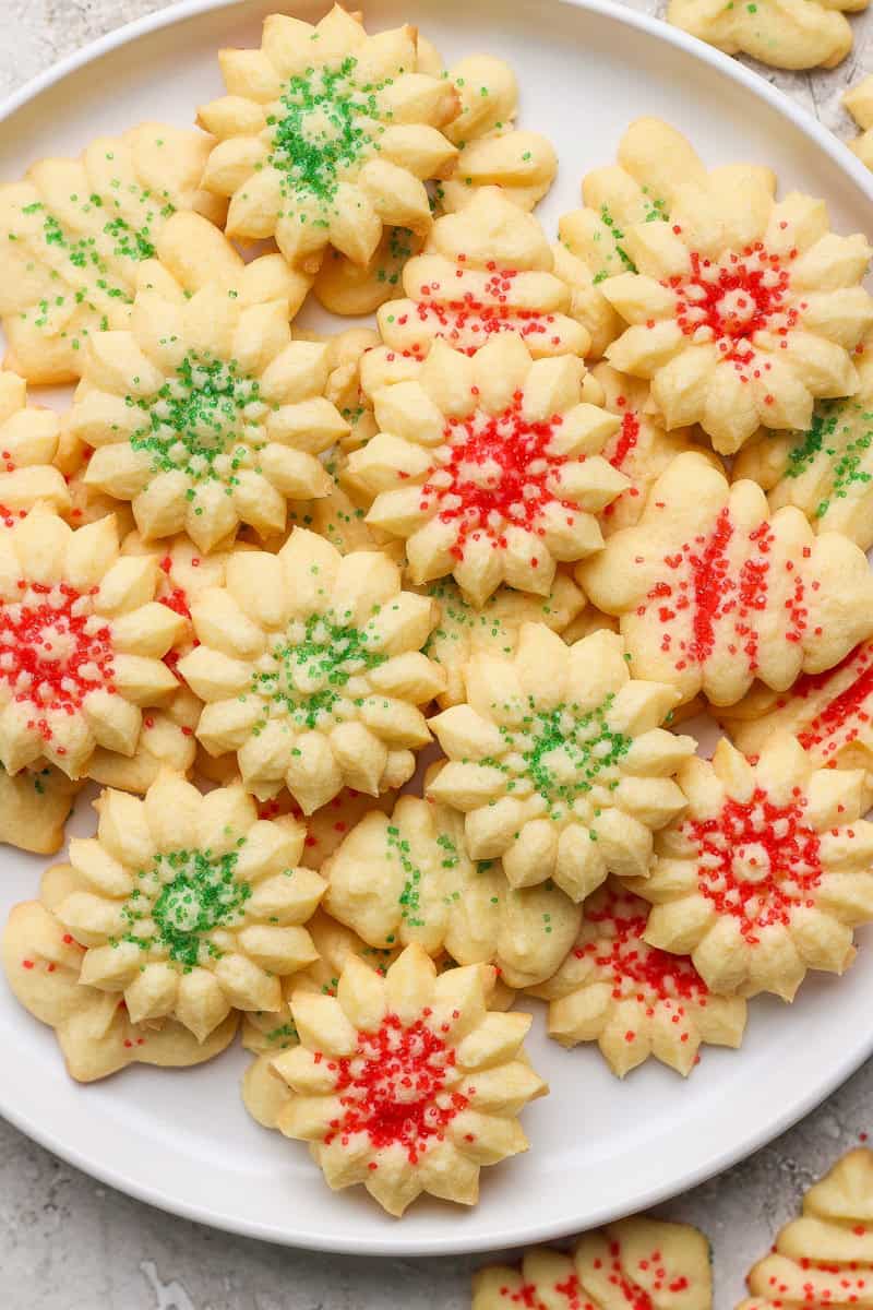 A plate of flower-shaped shortbread cookies decorated with green and red sprinkles.