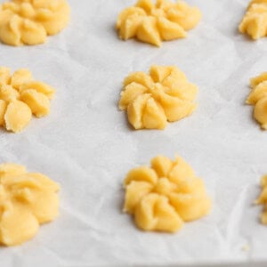 Raw cookie dough shaped into floral patterns on a parchment-lined baking sheet.