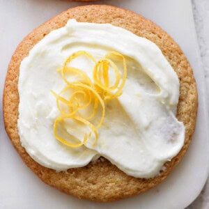 A lemon cookie adorned with cream cheese frosting and garnished with a twist of lemon peel.